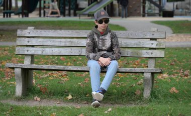 Parktaki bir çocuk parkta bankta oturuyor.,