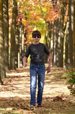 Küçük çocuk sonbahar parkında yürüyor.