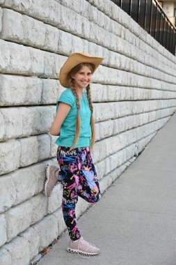 Şapkalı güzel sarışın kız tuğla duvarın yanında.,