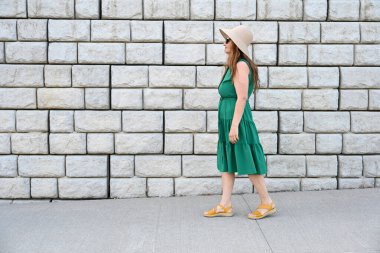 Yeşil şapkalı kadın tuğla duvarın yanında.,