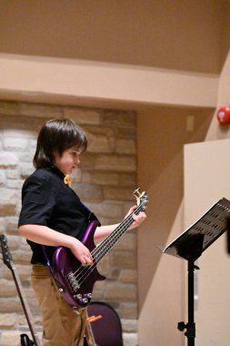 Siyah tişörtlü çocuk bas gitar çalıyor.,