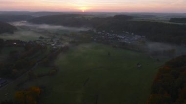 Lüksemburg 'daki sonbahar renkli ormanların ve vadilerin üzerinde sabah sisiyle kaplı hava aracı Sunrise View. 4k drone görüntüsü