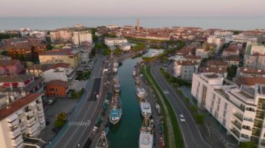 Venedik yakınlarındaki tatil köyü sahil kentinde bir Caorle 'un hava görüntüsü. Gün batımında gölde balıkçı tekneleri. 4k UHD Drone Videosu