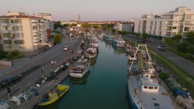 Venedik yakınlarındaki tatil köyü sahil kentinde bir Caorle 'un hava görüntüsü. Gün batımında gölde balıkçı tekneleri. 4k UHD Drone Videosu