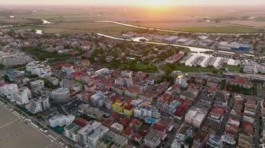 Venedik yakınlarındaki tatil köyü sahil kentinde bir Caorle 'un hava görüntüsü. Adriyatik Denizi 'nin gün batımında bir plajı. 4k UHD Drone Videosu
