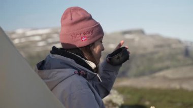 Kız Turist Sandviç yemekten ve çay içmekten zevk alıyor, Norveç 'te bir çadırın yanında oturuyor. Yürüyüşçü Sabah Yaşam Tarzı. Yüksek kalite 4k görüntü