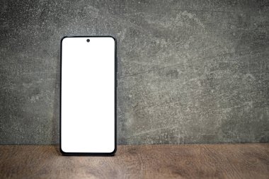 Boş beyaz ekran ve metin için alanı kopyalayan siyah akıllı telefon. Gri beton ve kahverengi ahşap masa.