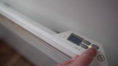 Duvara monte edilmiş elektrikli radyatör ısıtıcısı ayarlanıyor. Odadaki ısıyı düşüren bir adam. Avrupa 'da enerji krizi, artan ısıtma maliyeti kavramı.