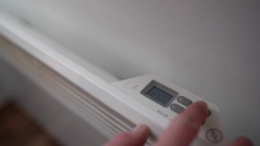 A man increasing temperature on wall mounted electric radiator heater in the room. Energy crisis in Europe, rising heating costs concept.