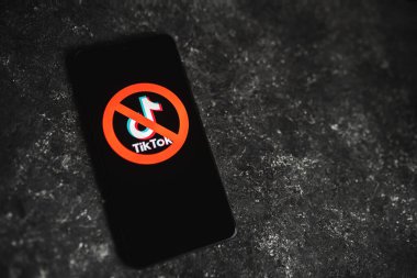 TikTok uygulamasının logosu, telefon ekranında kırmızı Ban işareti ile karalanmış. Tik Tok, ABD konseptinde yasaklandı. Fotokopi alanı olan koyu beton bir arka plan. Swansea, İngiltere - 15 Şubat 2023.