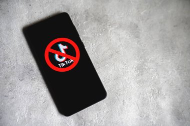 TikTok uygulamasının logosu, telefon ekranında kırmızı Ban işareti ile karalanmış. Tik Tok, ABD konseptinde yasaklandı. Kopya alanı olan somut bir arkaplan. Swansea, İngiltere - 15 Şubat 2023.