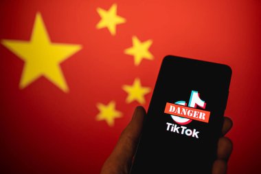 TikTok uygulama logosu Çin bayrağı arkaplanlı telefon ekranında kırmızı tehlike işareti ile çizilmiş. TikTok kişisel mahremiyet ve güvenlik için tehlikelidir. Swansea, İngiltere - 21 Şubat 2023.