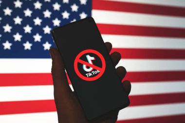 TikTok uygulamasının logosu kırmızı Ban işareti ile çizilmiş ve telefon ekranında ABD bayrağı arka planında sergilenmiş. TikTok 'un ABD konseptinde yasaklanması. Swansea, İngiltere - 21 Şubat 2023.