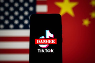 TikTok uygulamasının logosu kırmızı tehlike işareti ile işaretlenmiş ve telefon ekranında ABD ve Çin bayrakları var. ABD konseptinde Tik Tok yasağı. Swansea, İngiltere - 23 Şubat 2023.