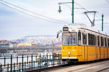 Famous yellow retro Tram line number 2 along Danube river in Budapest. Scenic tram ride with the Buda Hills view. Budapest, Hungary - January 29, 2023.