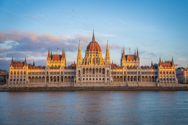 Budapest Parliament from across Danube river at Sunset, Hungary. Beautiful golden light on building rooftop. Evening sky with pink clouds.