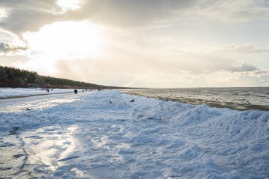 Kışın Baltık Denizi. Letonya, Jurmala yakınlarındaki karla kaplı plajda yürüyen insanlar.