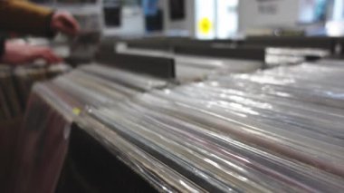 Müzik Vinili Plak Dükkanı. Ön plana odaklan. Arkaplanı bulanık. Dükkanda Vinyls 'i izleyen adamlar var. Eski usul, 4K 'lık ses kaydı..