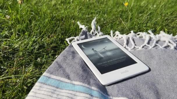 Λευκό Amazon Kindle Book Reader Στην Κουβέρτα Πικνίκ Στο Γρασίδι — Αρχείο Βίντεο