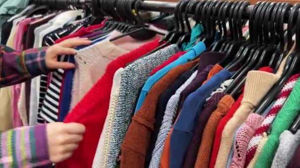 Ένας Νεαρός Αγοράζει Ρούχα Από Μεταχειρισμένο Μαγαζί Κρεμάστρες Πολύχρωμα Πουλόβερ — Αρχείο Βίντεο