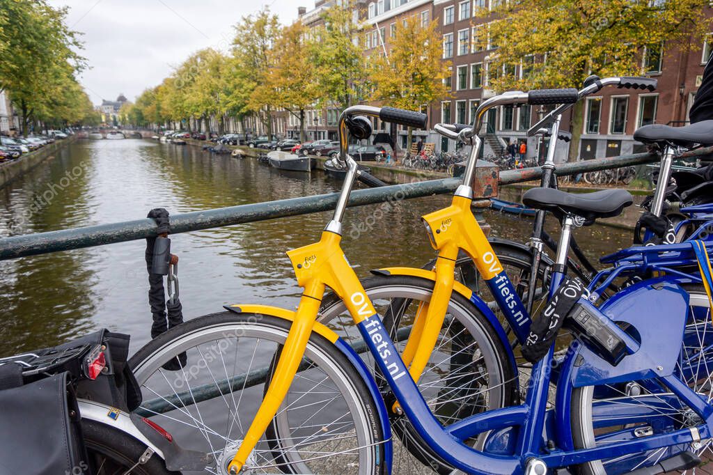 OV-fiets rental bike from NS, the Dutch train company. Yellow and blue bicycle parked on bridge of Amsterdam canal. Amsterdam, the Netherlands - October 23, 2023