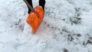 Kar yağarken bahçede turuncu bir kürekle kar küreyen biri. Elle kar temizleme ya da temizleme. Kış bakım kavramı,