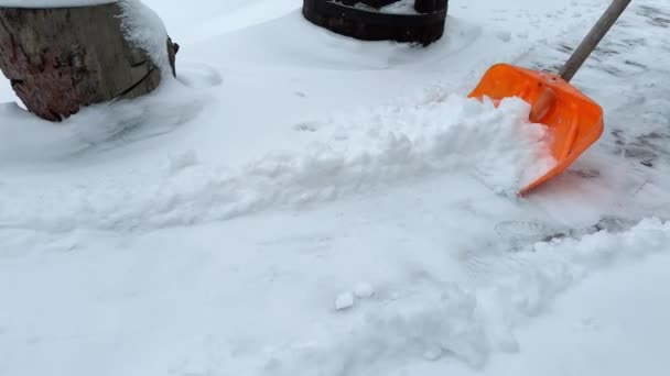手動の雪の取り外しまたはクリア 雪が降ったときに庭にオレンジ色のシャベルで雪を降らせる人 冬季メンテナンスコンセプト — ストック動画