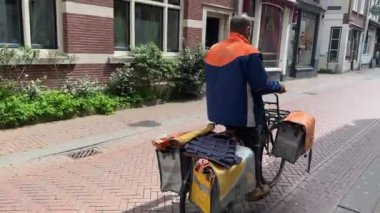 Bisikletli postacı, üzerinde logo bisikleti olan turuncu eyer çantalarıyla Haarlem 'de posta dağıtıyordu. Hollandalı posta şirketi ve teslimat servisi. Haarlem, Hollanda - 21 Haziran 2024.