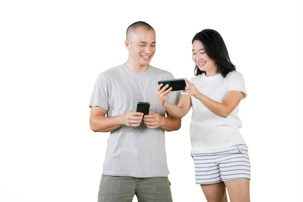 一对快乐的年轻夫妇站在演播室里 一边看手机上有趣的内容 因白人背景而被隔离 — 图库照片