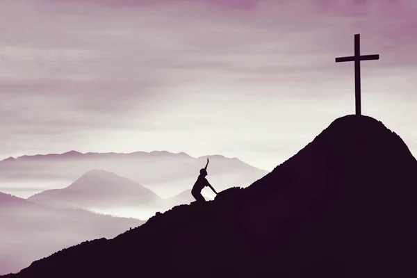 年轻男子在山上爬行的轮廓朝向有雾蒙蒙的早晨背景的十字标志 — 图库照片