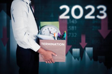 İş adamı elinde fesih sözcüğüyle bir kutu tutarken 2023 'te azalan finans okuyla ayakta duruyor.