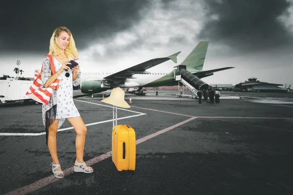 年轻的金发女子站在机场 站在乌云密布的天空中 看着护照和车票 — 图库照片