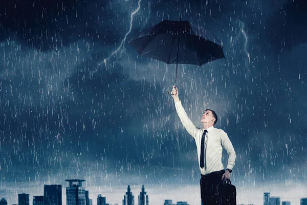 雨の嵐の中で傘を持って街並を背景に立つ白人実業家 — ストック写真