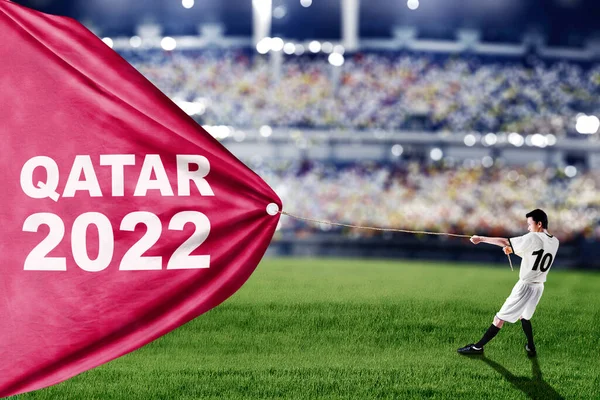 スタジアムに立っている間 カタール2022テキストでファブリックを引くためにチェーンを使用して男性サッカー選手の側面図 — ストック写真