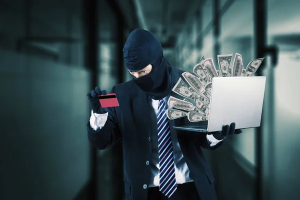 黑客身穿西服 戴着黑色面具 手持手提电脑 从信用卡里偷钱 — 图库照片