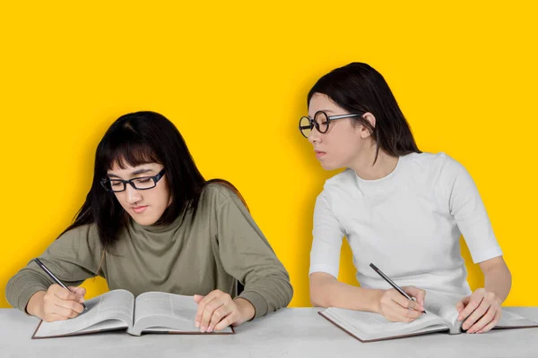 黄色の背景に隔離された試験中に同級生の教科書を覗き見する若いアジアの学生のイメージ — ストック写真