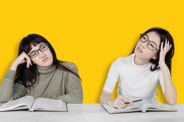 Exhausted and bored students with glasses preparing for exams isolated on yellow background