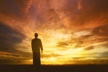 Müslüman adam güneşin doğuşunda ya da batışında elinde bilezik tutarak namaz kılıyor.