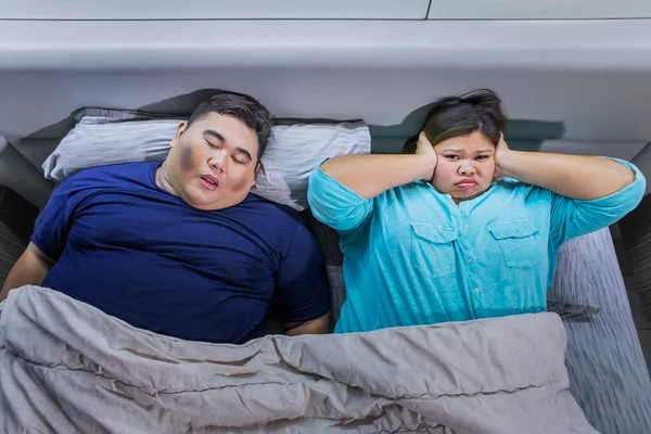 ベッドの中で太りすぎのカップル夜に眠っている女性と彼女の耳を閉じる彼女の耳は男がいびきを聞いて疲れて — ストック写真