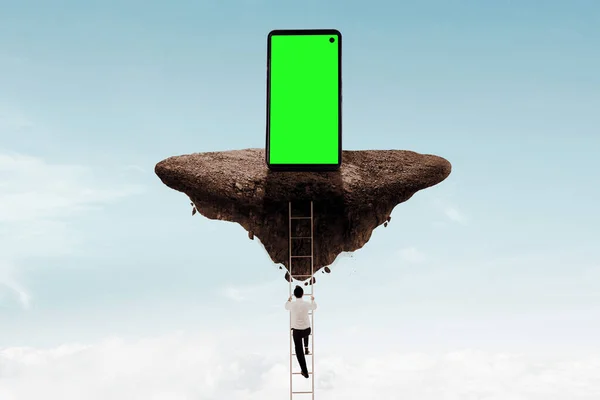 商人爬上一个小飞岛 在上面带着空白的绿色屏幕 拿着手机 — 图库照片