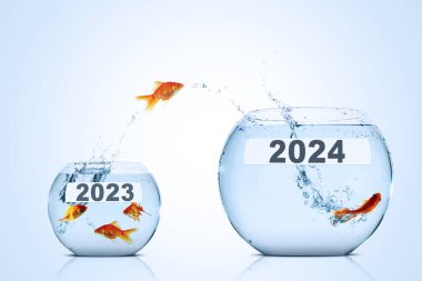 Altın balık daha küçük bir akvaryumdan daha büyük bir akvaryuma atlıyor ve mavi zemin üzerinde 2024 yeni yıl rakamı var.