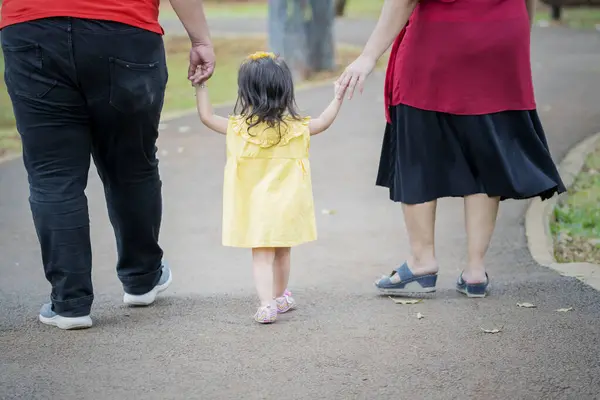 Back view of obese parents walking with their daughter in the park