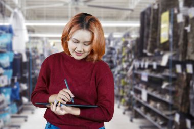 Genç, şık bir kadın, depo geçmişi olan bir stil ile yazarken dijital tablete sarılıyor.