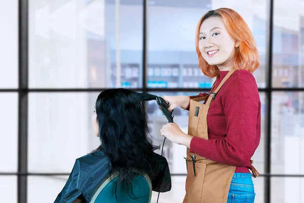 Asian hairdresser brushing her clients red hair with little comb brush and getting it ready for a cut