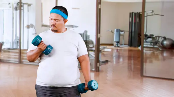 Overweight man training with dumbbells in a private gym