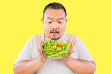 Şişman Asyalı adam sarı arka planda taze yeşil salata tutuyor.