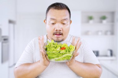 Şişko Asyalı adam mutfakta taze sebze salatası tutuyor.