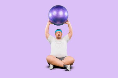 Mor arka planda izole edilmiş spor topuyla egzersiz yapan kilolu adam.