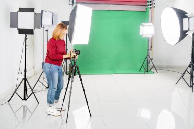 Genç Asyalı kadın fotoğrafçı fotoğraf stüdyosuna kamera ve tripodu yerleştiriyor.