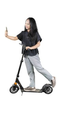 Cep telefonlu bir kız öğrencinin beyaz arka planda izole edilmiş elektrikli scooterla selfie çekerken tam boy profil fotoğrafı.